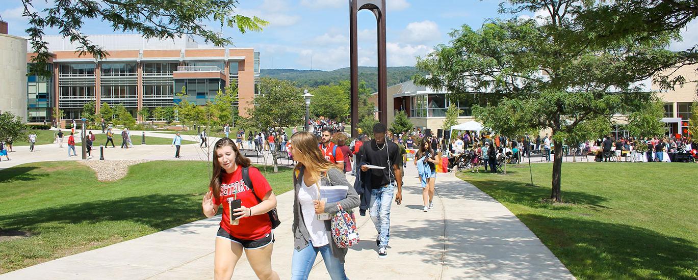 A large group of Frostburg State students walk to class near the campus clocktower on a warm, sunny day